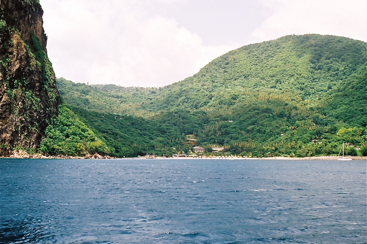 A tropical Caribbean island coastline with green hills and clear blue water